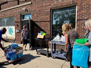 two females and one male use carts to transport the donations into the building as a third female holds the door open.